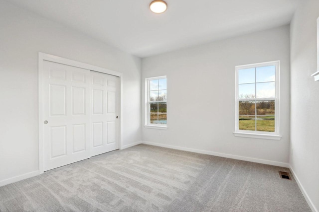 unfurnished bedroom featuring multiple windows, light carpet, and a closet