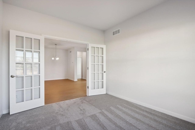 carpeted empty room with a notable chandelier and french doors