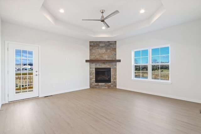 unfurnished living room featuring a raised ceiling, ceiling fan, a fireplace, and light hardwood / wood-style floors