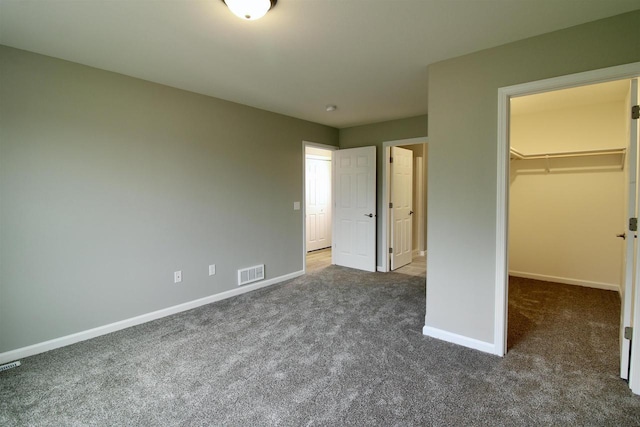 unfurnished bedroom with dark carpet, a spacious closet, and a closet