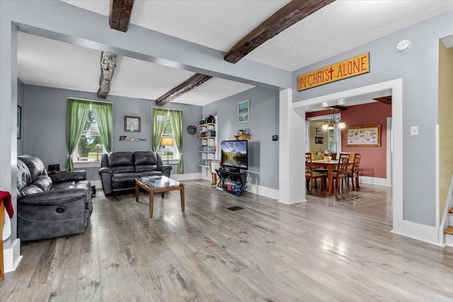 living room featuring beamed ceiling, wood-type flooring, and a textured ceiling