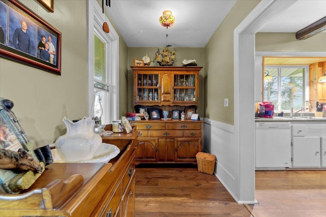 bar featuring white dishwasher, sink, and hardwood / wood-style flooring