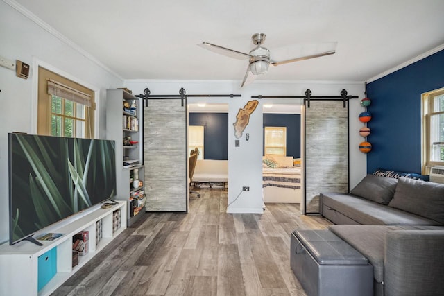 living room featuring a barn door, hardwood / wood-style flooring, ceiling fan, and ornamental molding