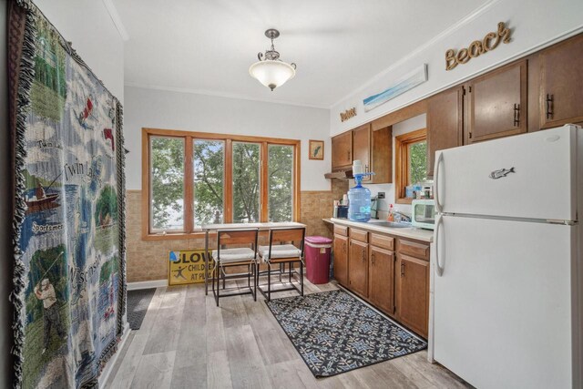 kitchen with white appliances, light wood-type flooring, tile walls, ornamental molding, and decorative light fixtures