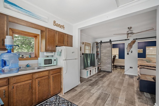 kitchen with white appliances, light hardwood / wood-style flooring, ceiling fan, a barn door, and ornamental molding