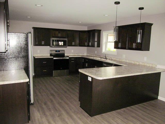 kitchen with kitchen peninsula, stainless steel appliances, dark wood-type flooring, sink, and decorative light fixtures