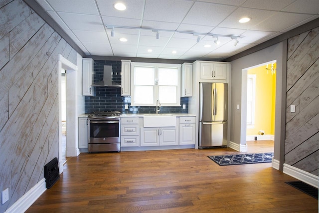 kitchen with appliances with stainless steel finishes, sink, wall chimney range hood, dark hardwood / wood-style floors, and white cabinetry