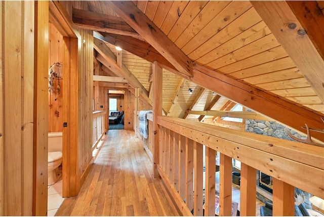 corridor featuring vaulted ceiling with beams, light wood-type flooring, wooden ceiling, and wood walls