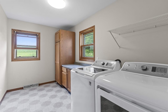 clothes washing area featuring cabinets, a wealth of natural light, and washer and clothes dryer