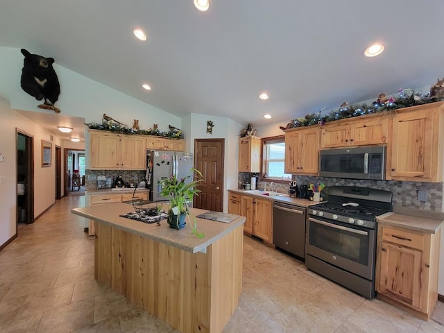 kitchen featuring stainless steel appliances, an island with sink, vaulted ceiling, decorative backsplash, and light brown cabinetry