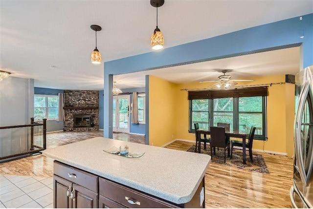 kitchen with ceiling fan, hanging light fixtures, a brick fireplace, stainless steel fridge, and a kitchen island