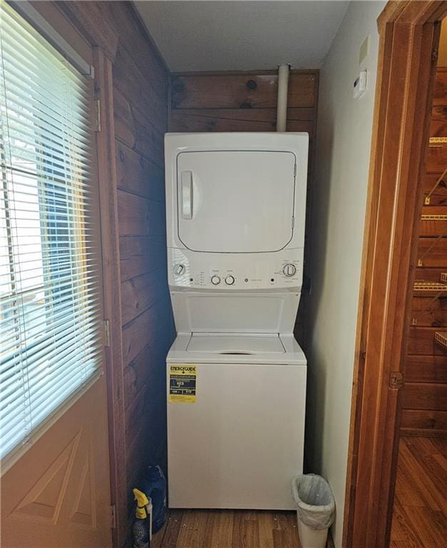 laundry room with dark wood-type flooring, wooden walls, and stacked washer and clothes dryer