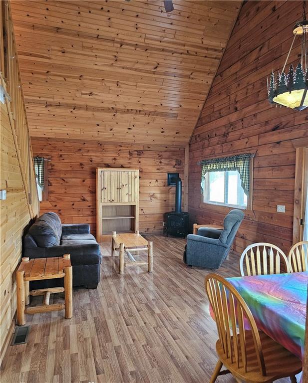 living room with wood ceiling, wood-type flooring, high vaulted ceiling, a wood stove, and wood walls