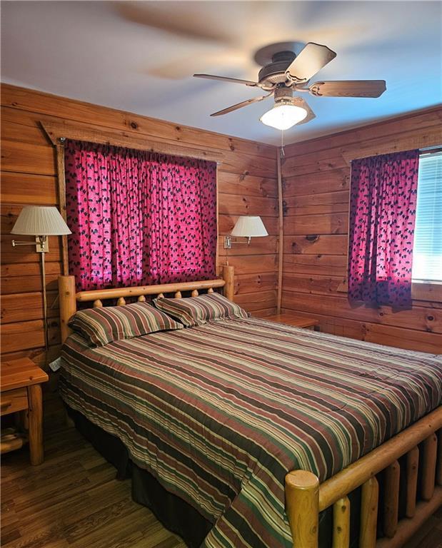 bedroom with dark hardwood / wood-style flooring, ceiling fan, and wooden walls