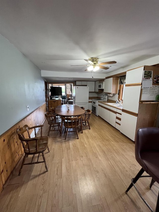 dining room with light hardwood / wood-style floors, ceiling fan, wooden walls, and sink