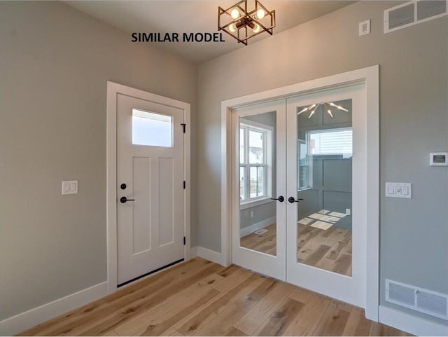 entrance foyer featuring french doors, light hardwood / wood-style floors, and an inviting chandelier