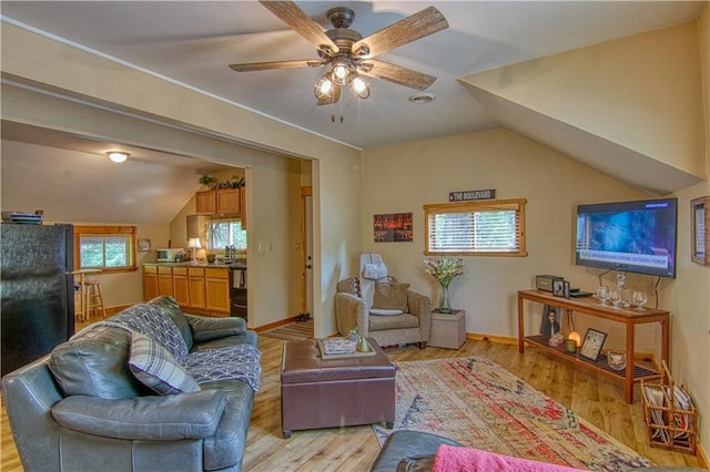 living room with ceiling fan, plenty of natural light, vaulted ceiling, and light wood-type flooring