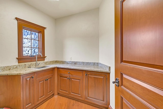 kitchen featuring light wood-type flooring, light stone countertops, and sink