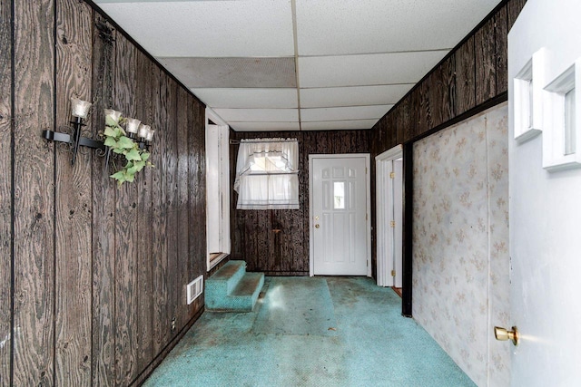 entryway featuring wood walls, a drop ceiling, and carpet floors