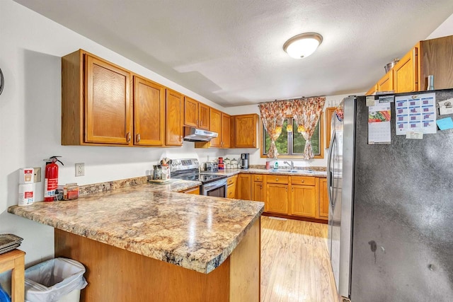 kitchen featuring sink, light hardwood / wood-style flooring, a textured ceiling, kitchen peninsula, and stainless steel appliances