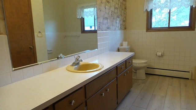 bathroom featuring baseboard heating, wood-type flooring, toilet, vanity, and tile walls