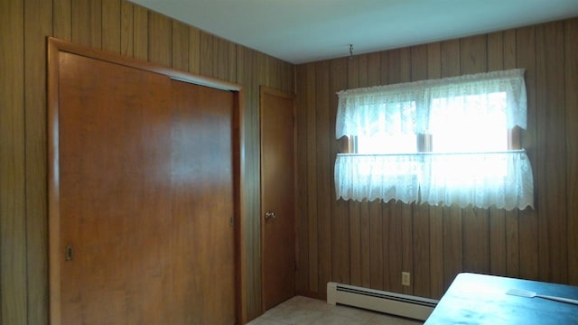 bedroom featuring baseboard heating, light tile patterned flooring, a closet, and wood walls