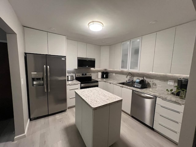 kitchen with stainless steel appliances, sink, a center island, white cabinetry, and backsplash