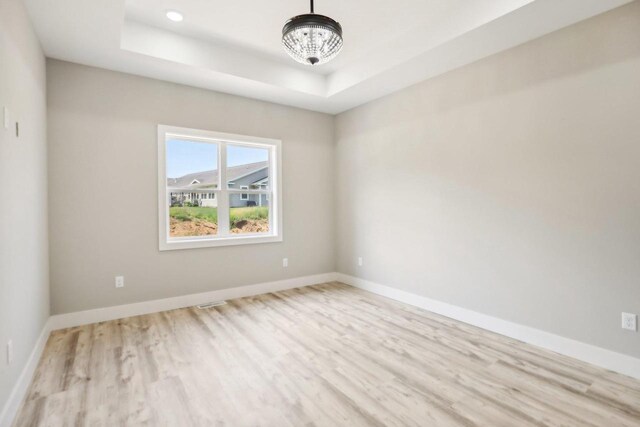 unfurnished room featuring light wood-type flooring and a tray ceiling