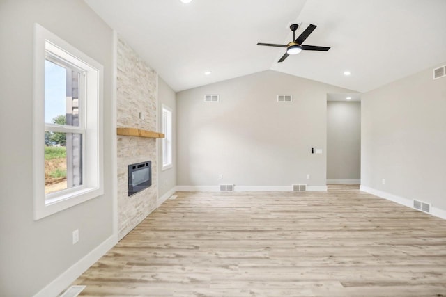 unfurnished living room with a stone fireplace, vaulted ceiling, light wood-type flooring, and ceiling fan