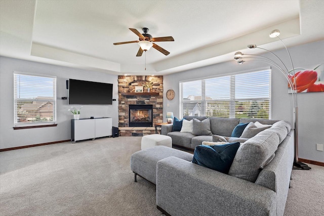 living room with a stone fireplace, carpet flooring, a tray ceiling, and ceiling fan