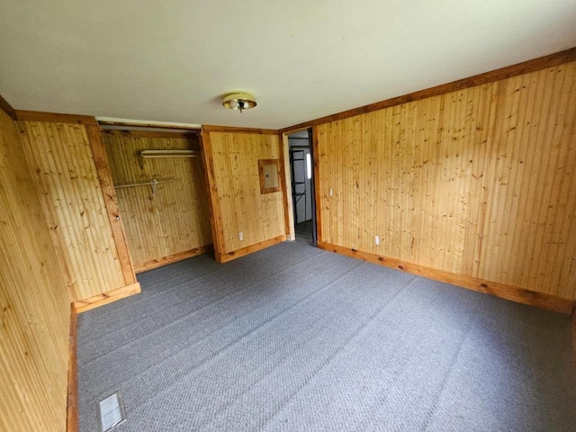 unfurnished bedroom with wooden walls, a closet, and dark colored carpet