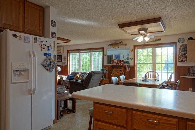 kitchen featuring ceiling fan, an AC wall unit, white refrigerator with ice dispenser, and a textured ceiling