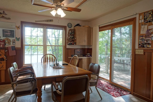 dining space featuring ceiling fan, a textured ceiling, and wooden walls