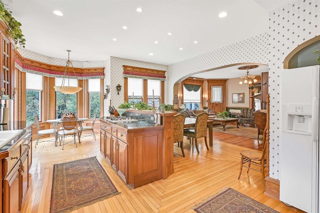 kitchen featuring an inviting chandelier, hanging light fixtures, stainless steel gas cooktop, light wood-type flooring, and white refrigerator with ice dispenser