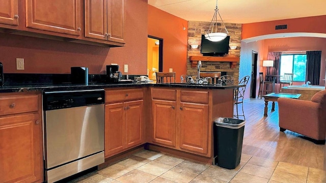 kitchen featuring dishwasher, dark stone countertops, kitchen peninsula, hanging light fixtures, and light tile patterned floors