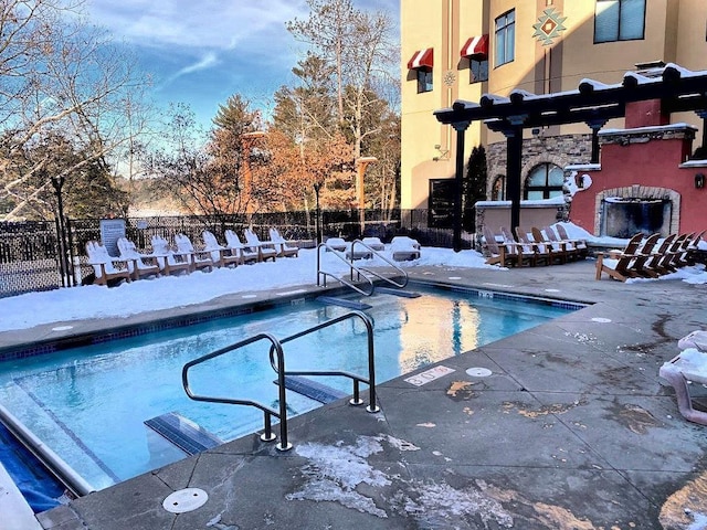 snow covered pool with a patio and an outdoor brick fireplace