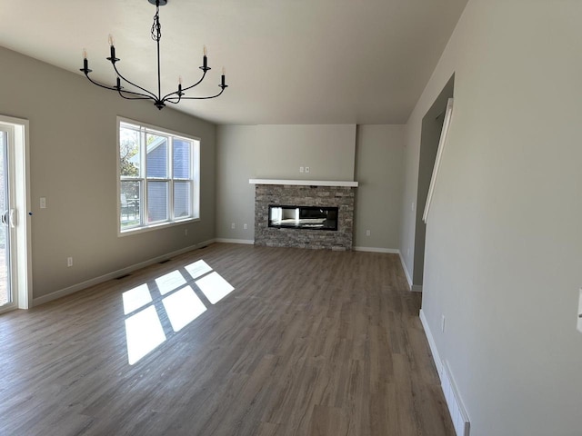 unfurnished living room with an inviting chandelier, a stone fireplace, and hardwood / wood-style flooring