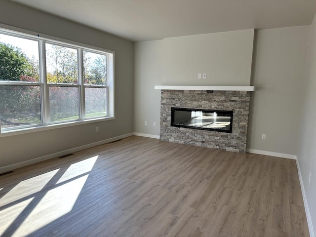 unfurnished living room with hardwood / wood-style floors and a stone fireplace