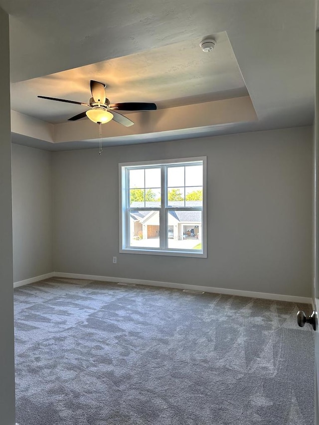 spare room with ceiling fan, a tray ceiling, and carpet flooring