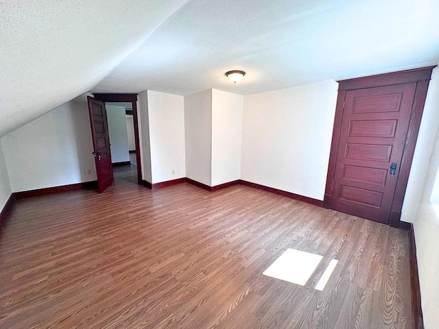 additional living space featuring a textured ceiling, dark hardwood / wood-style flooring, and vaulted ceiling