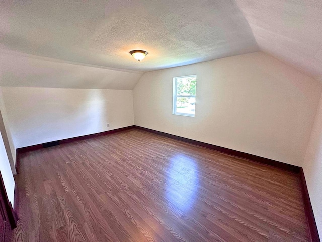 additional living space with vaulted ceiling, dark hardwood / wood-style floors, and a textured ceiling