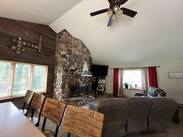 living room featuring lofted ceiling, a stone fireplace, ceiling fan, and wood walls