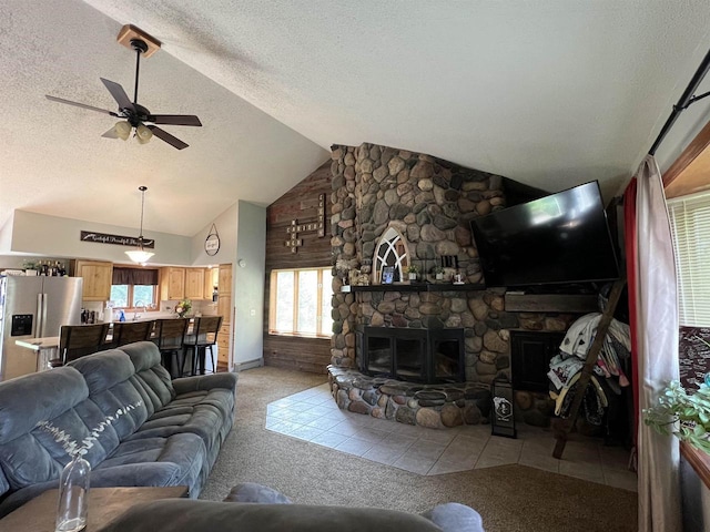 tiled living room featuring ceiling fan, a stone fireplace, vaulted ceiling, and a textured ceiling