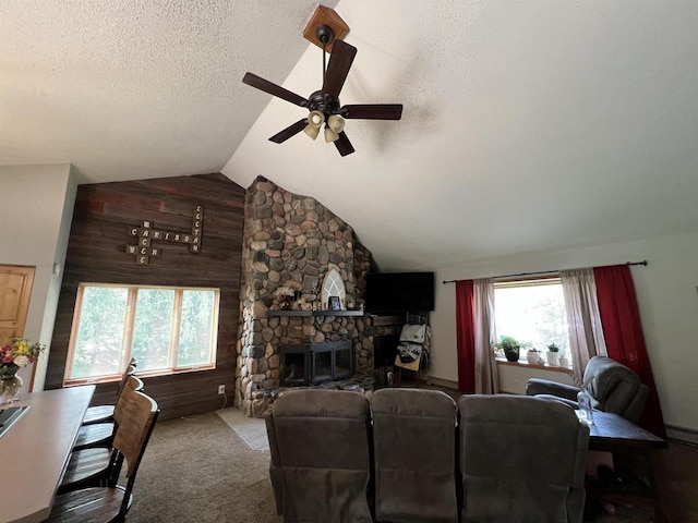 living room with lofted ceiling, ceiling fan, wooden walls, a textured ceiling, and a stone fireplace