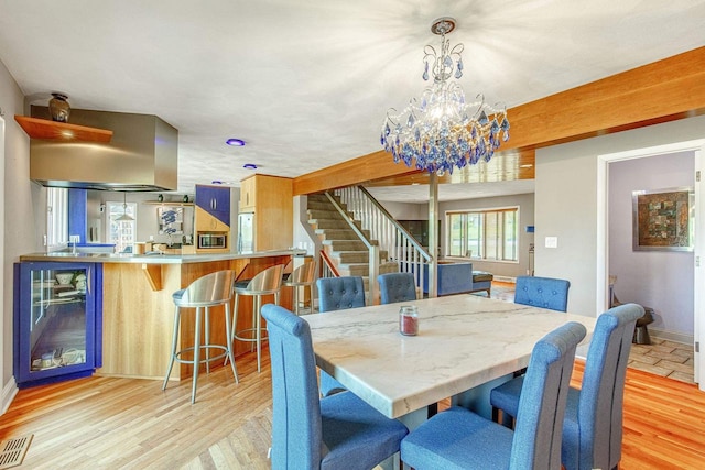 dining space featuring wine cooler, an inviting chandelier, bar, and light hardwood / wood-style floors