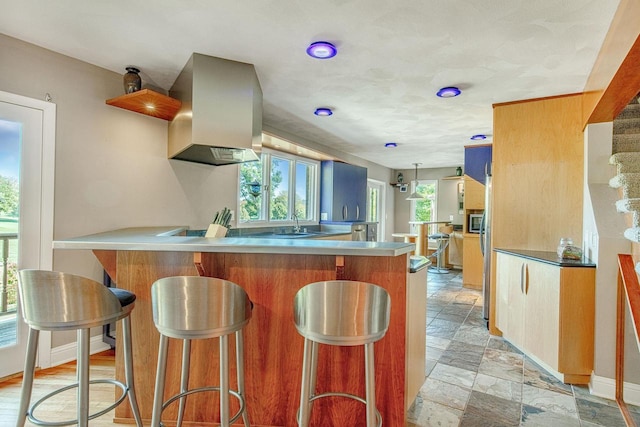 kitchen featuring island range hood, kitchen peninsula, stainless steel microwave, a breakfast bar area, and sink