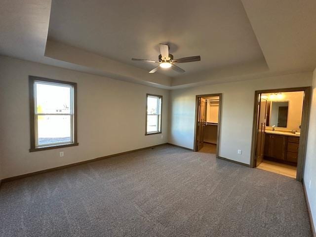 unfurnished bedroom featuring a raised ceiling, multiple windows, a spacious closet, connected bathroom, and a closet