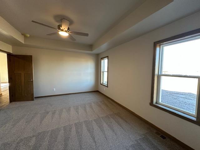 unfurnished room featuring carpet floors, a tray ceiling, and ceiling fan