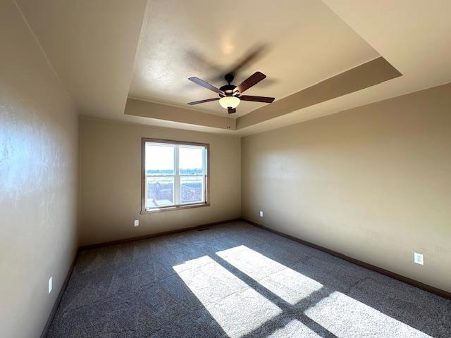 empty room featuring ceiling fan, carpet flooring, and a raised ceiling