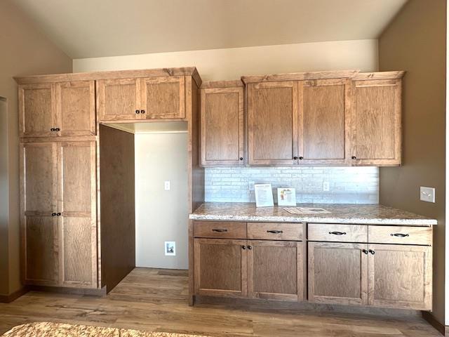 kitchen with backsplash, vaulted ceiling, light wood-style flooring, and light stone countertops